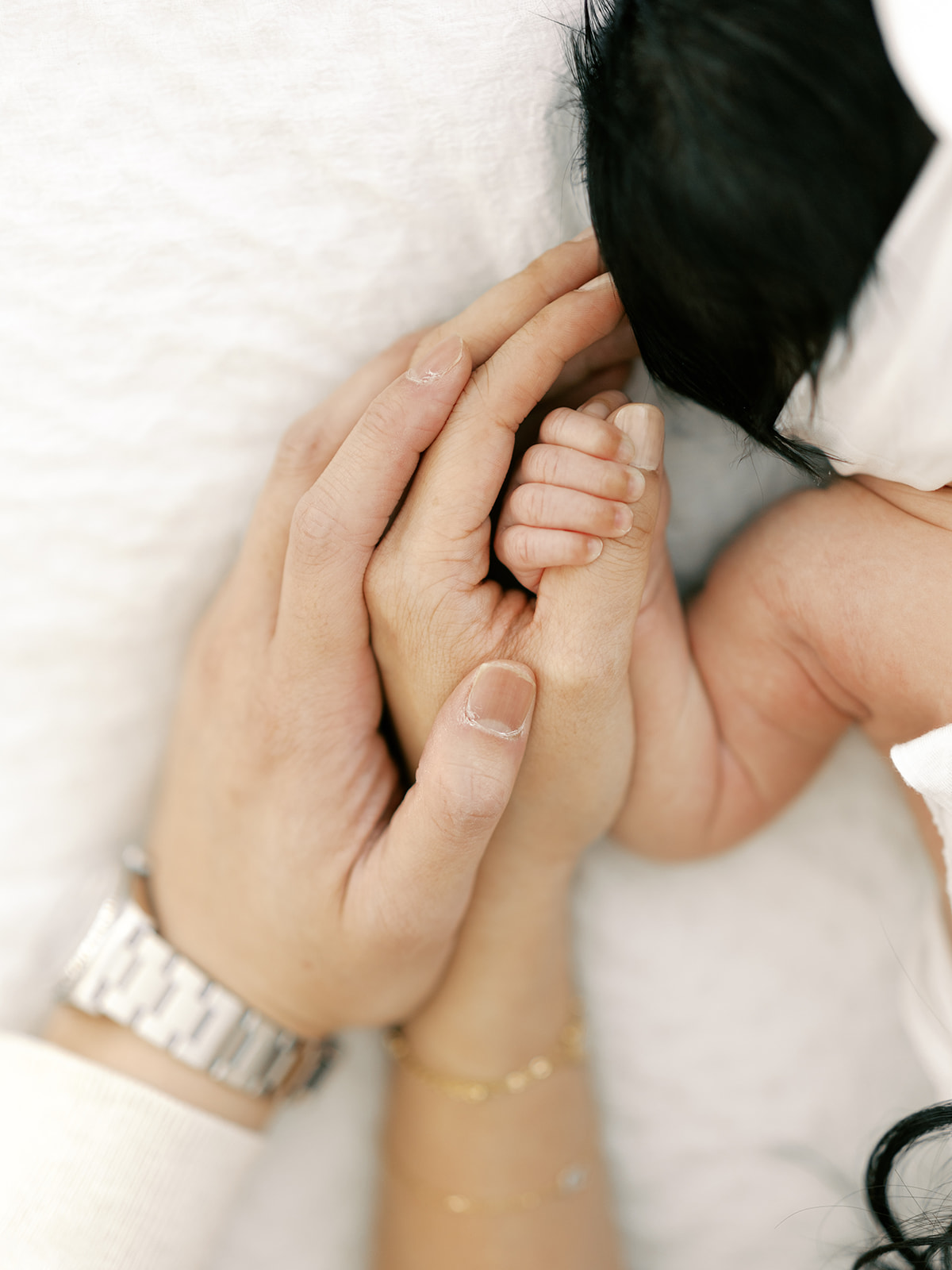 Details of a newborn's hand holding mom's thumb with dad's hand on hers after visiting Minneapolis baby stores