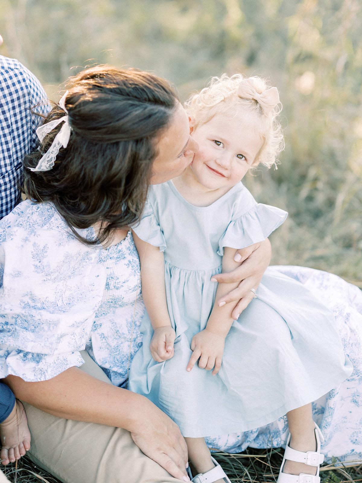 A mom kisses her toddler daughter in a blue dress in her lap before visiting indoor playgrounds in Minneapolis