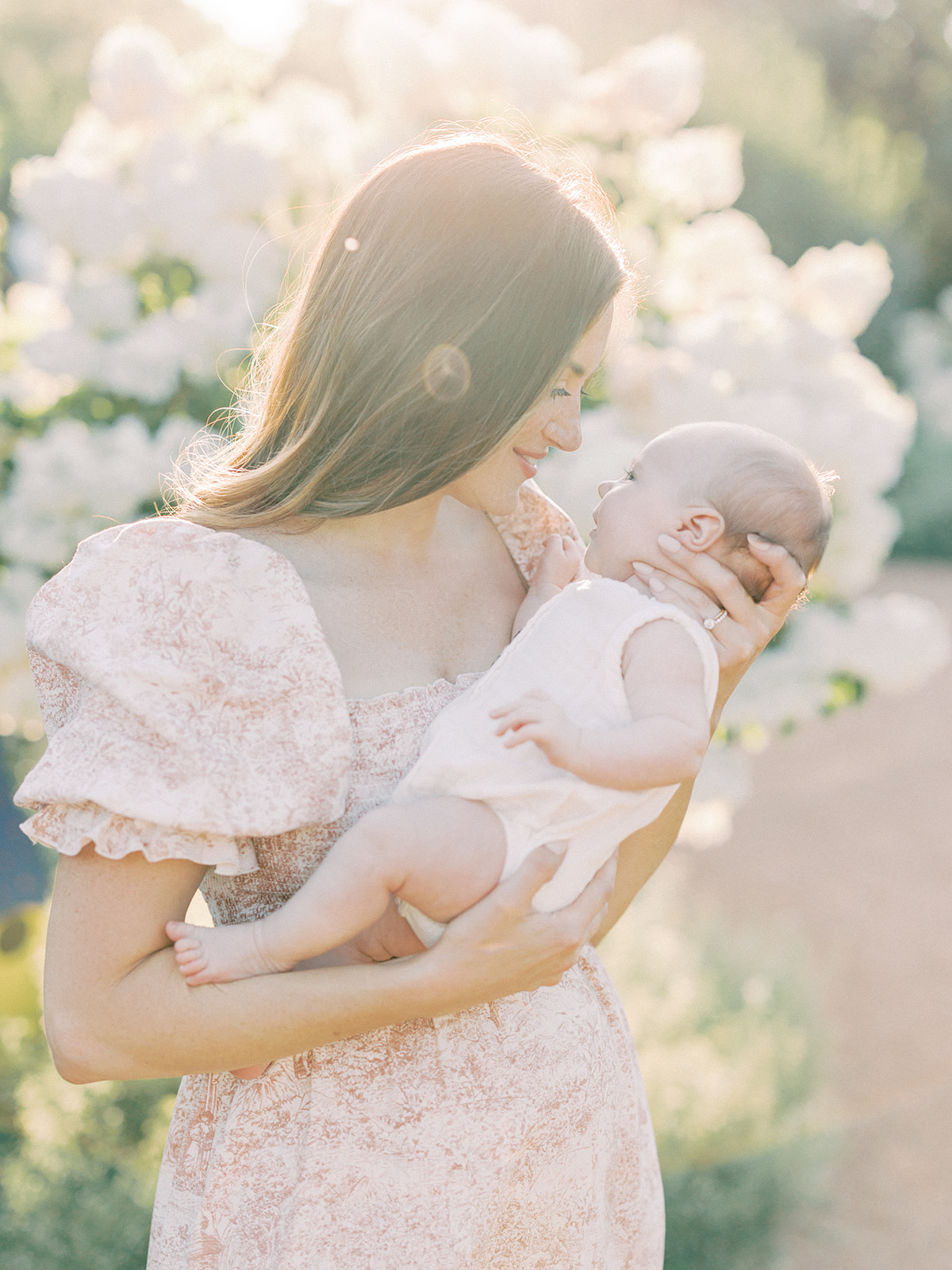 A happy new mom cradles her baby in a garden at sunset in a pink dress after meeting lactation consultants in Minneapolis