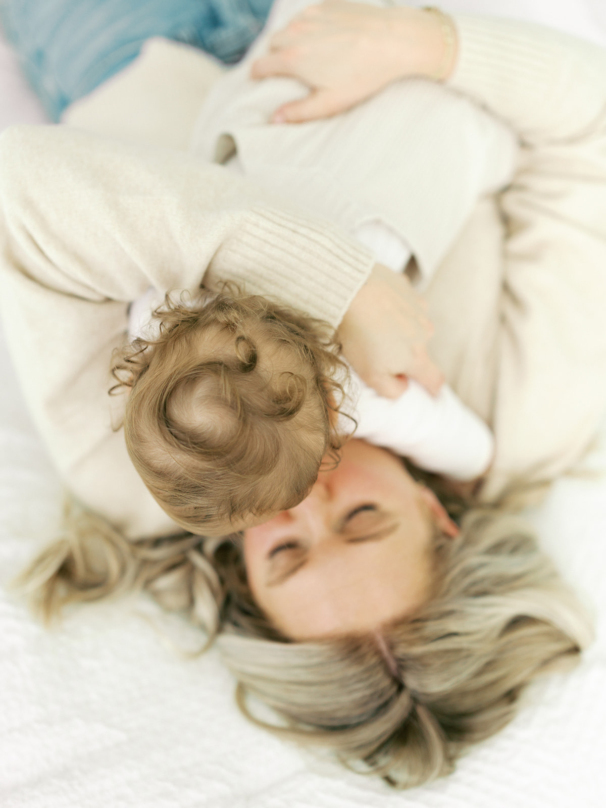 A look down on a baby laying on mom's chest while playing on a bed