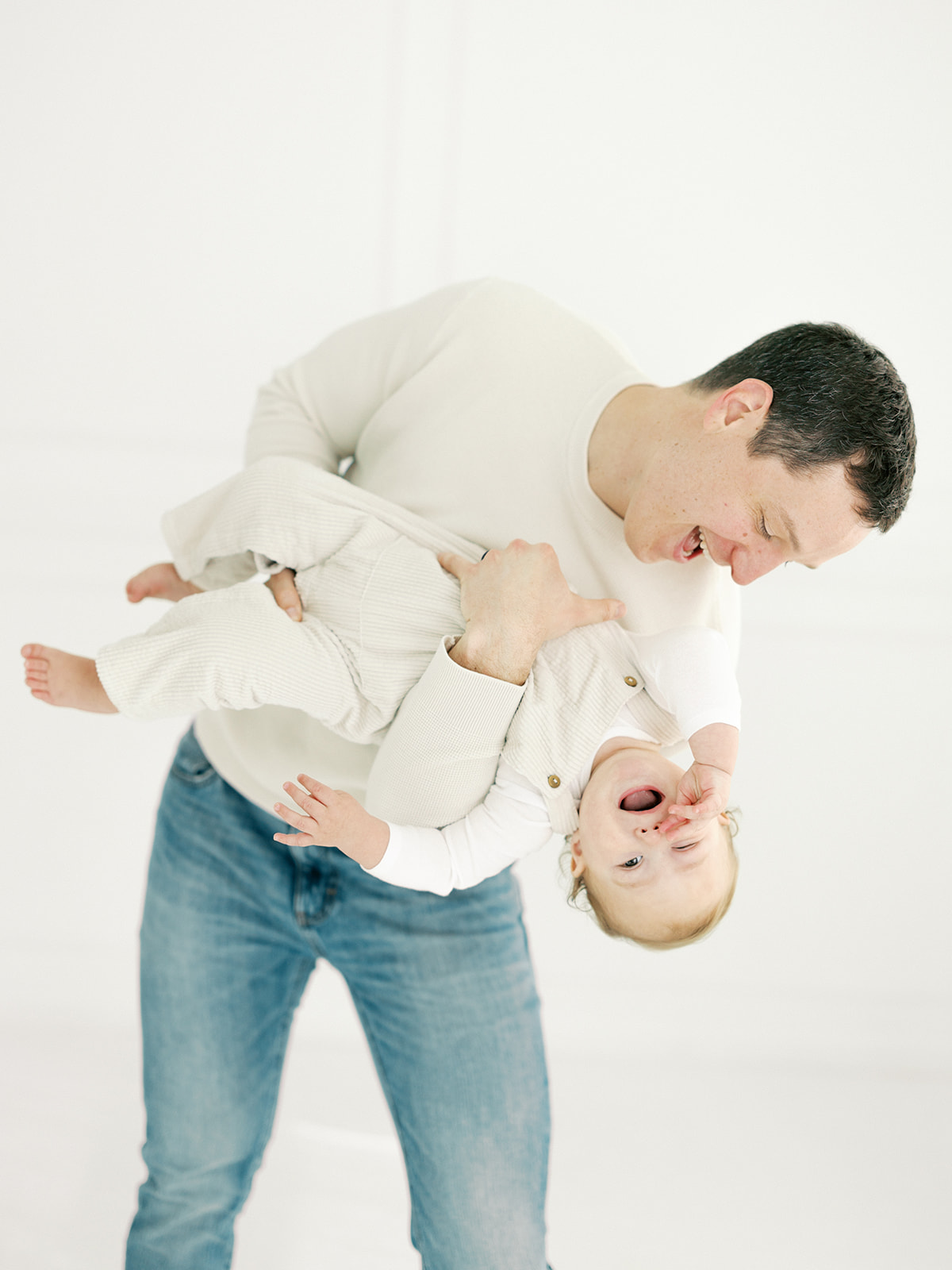 A laughing dad flips his giggling baby upside down in a studio after meeting Minneapolis Midwives