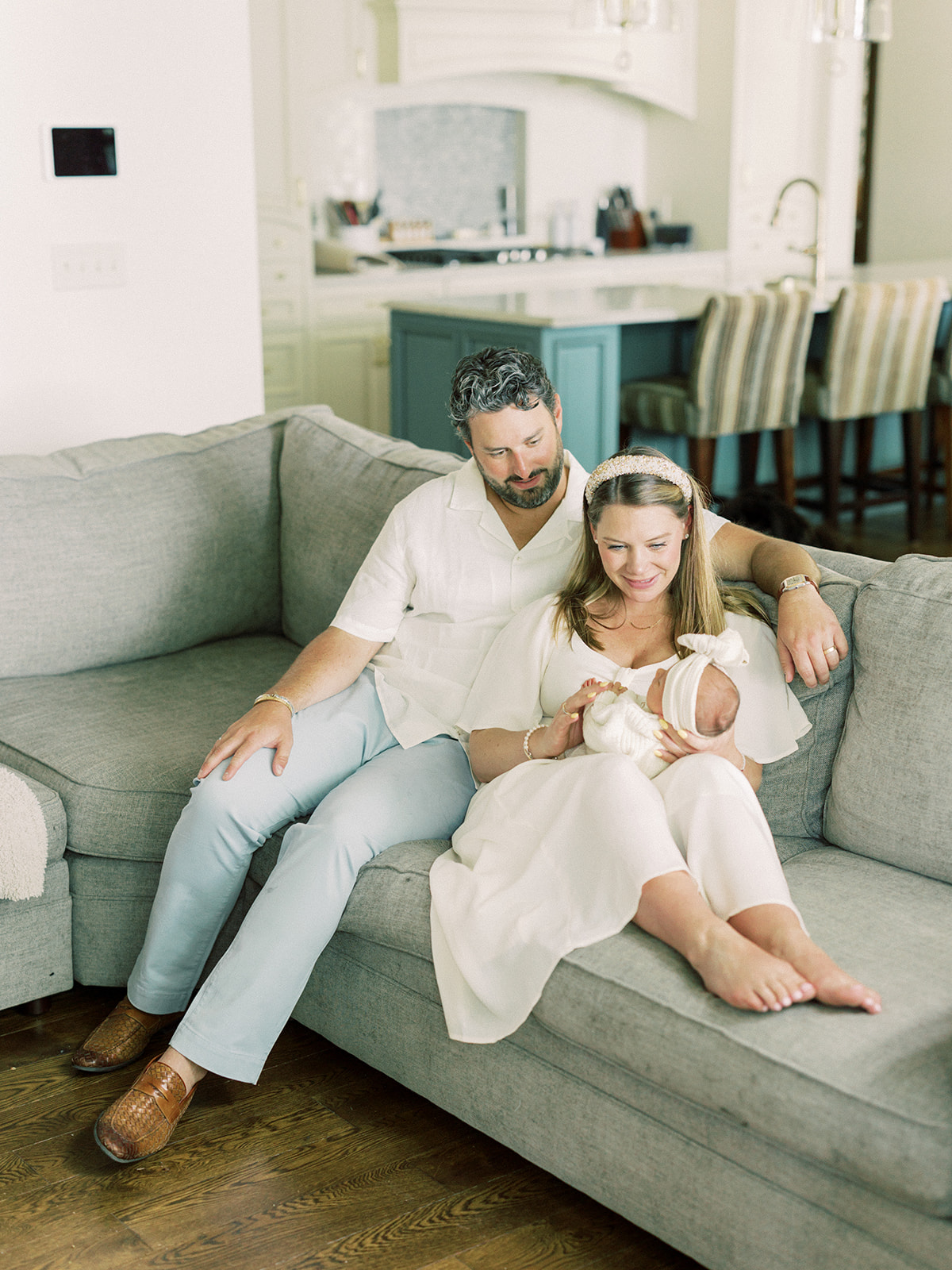 A newborn lays in mom's lap as she sits across a couch leaning in dad in white after finding new mom groups in Minneapolis