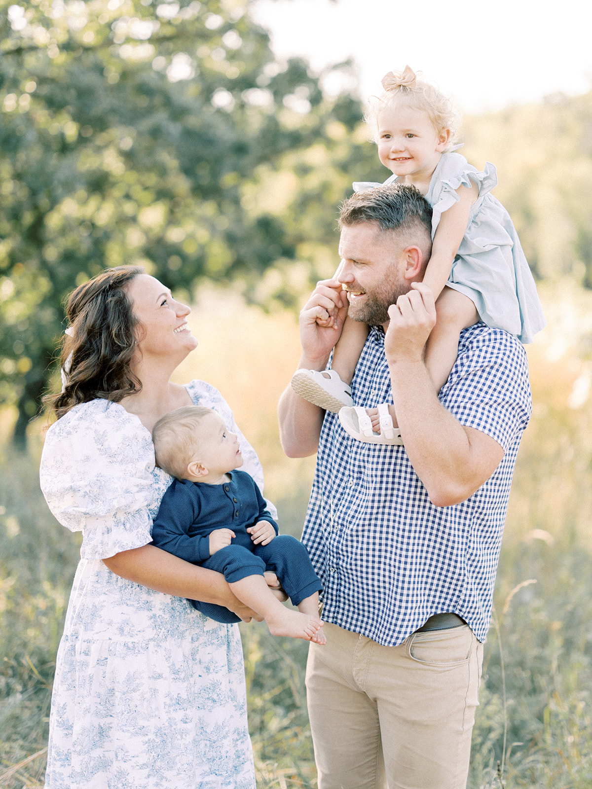 Happy mom and dad play with their baby son and daughter in a park at sunset