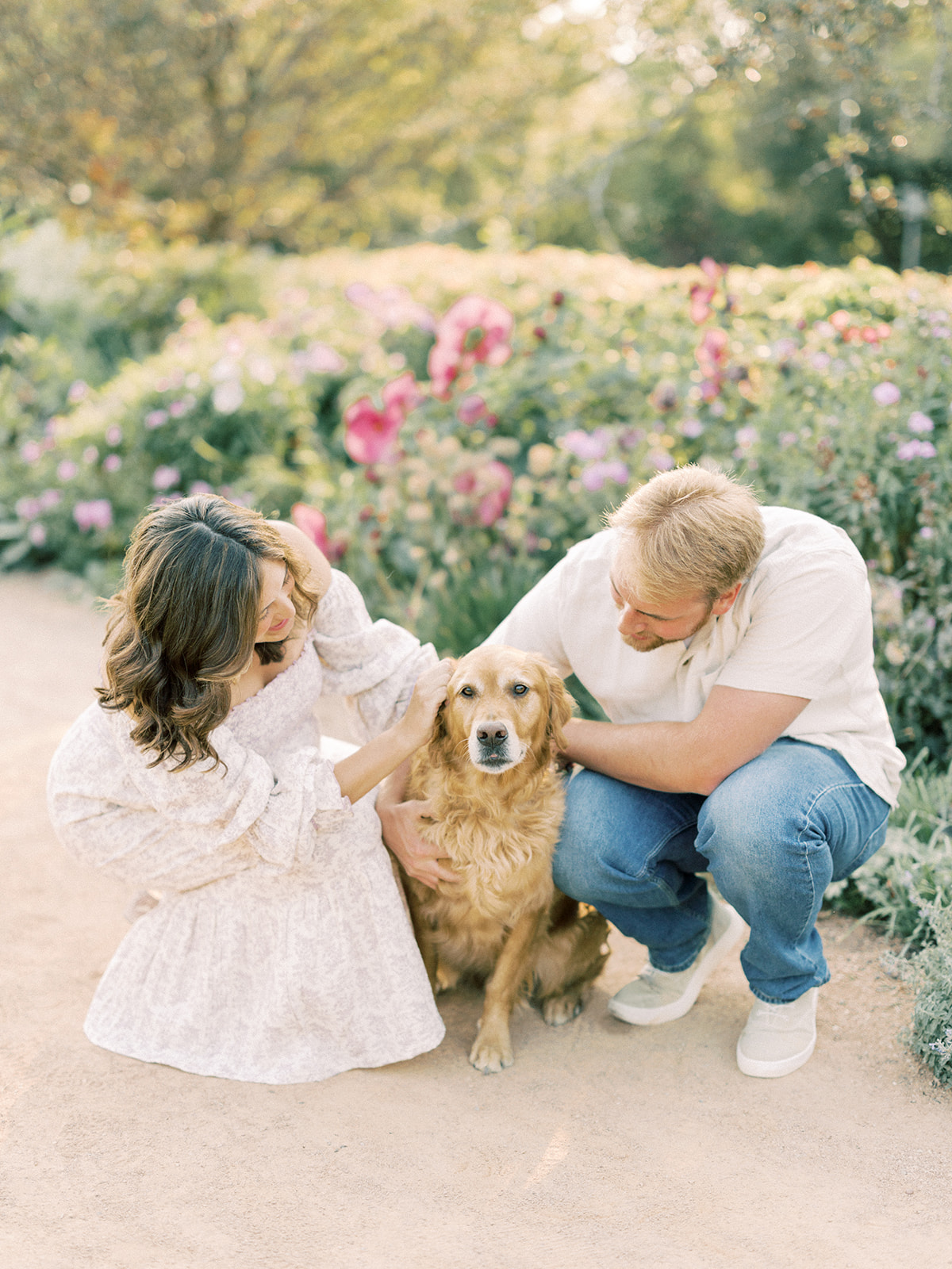 A happy couple pet and hug their dog in a flower garden at sunset in white at one of the photoshoot locations in Minneapolis